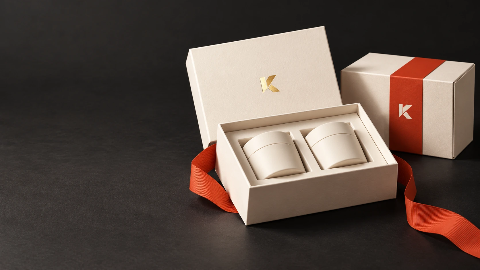 Geöffnete cremefarbene Premiumbox mit passendem Papierinlay, zwei Produktdosen und goldfarbenem K-Signet